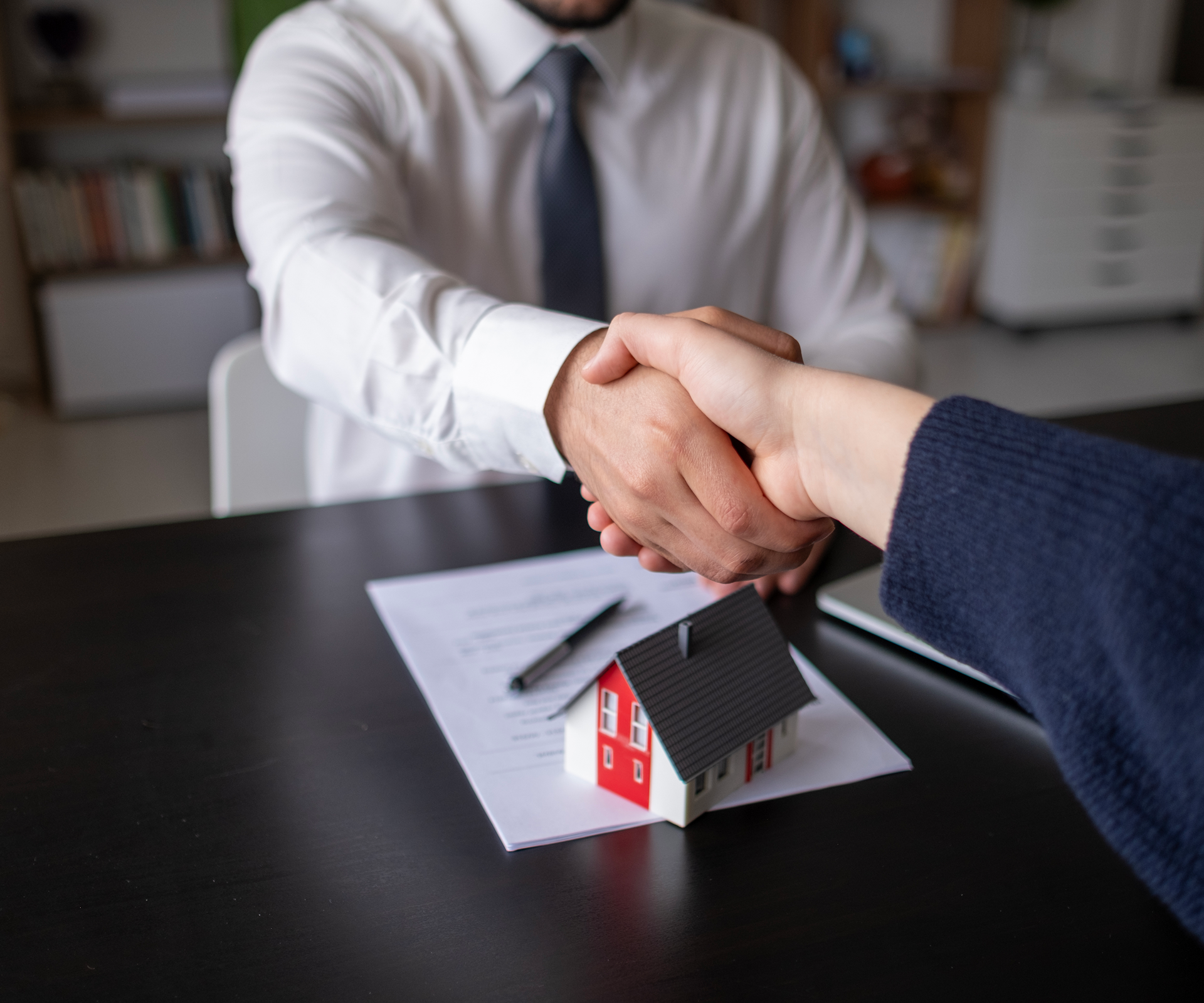 Handshake over real estate contract and model house.